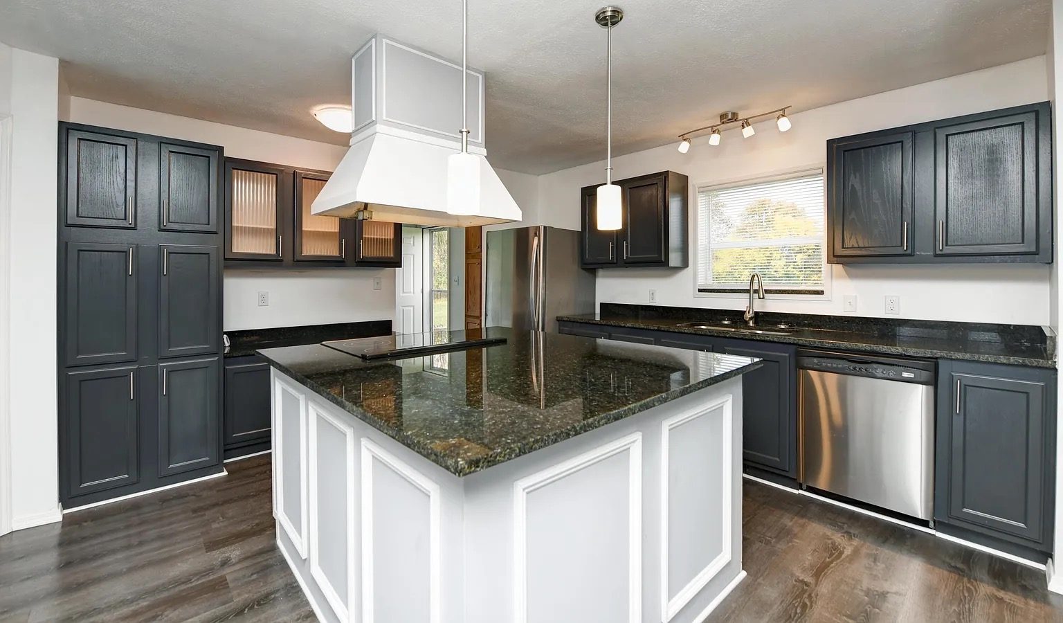 Finished kitchen with dark cabinets, a granite island with white panelled sides, and a white range hood